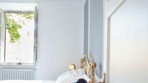 Ein Schlafzimmer mit einem Bett, einem Nachttisch mit Lampe und einem Fenster mit Blick auf Grünflächen.