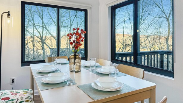 A dining area with a table set for four, large windows, and a vase with red flowers. - Nature Views Washer, Dryer, Balcony 1 Purg #6 (Vernon)