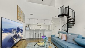 A modern living room with a large flat-screen TV, a blue sofa, a coffee table, and a spiral staircase. - Nature Views Washer, Dryer, Balcony 1 Purg #6 (Vernon)