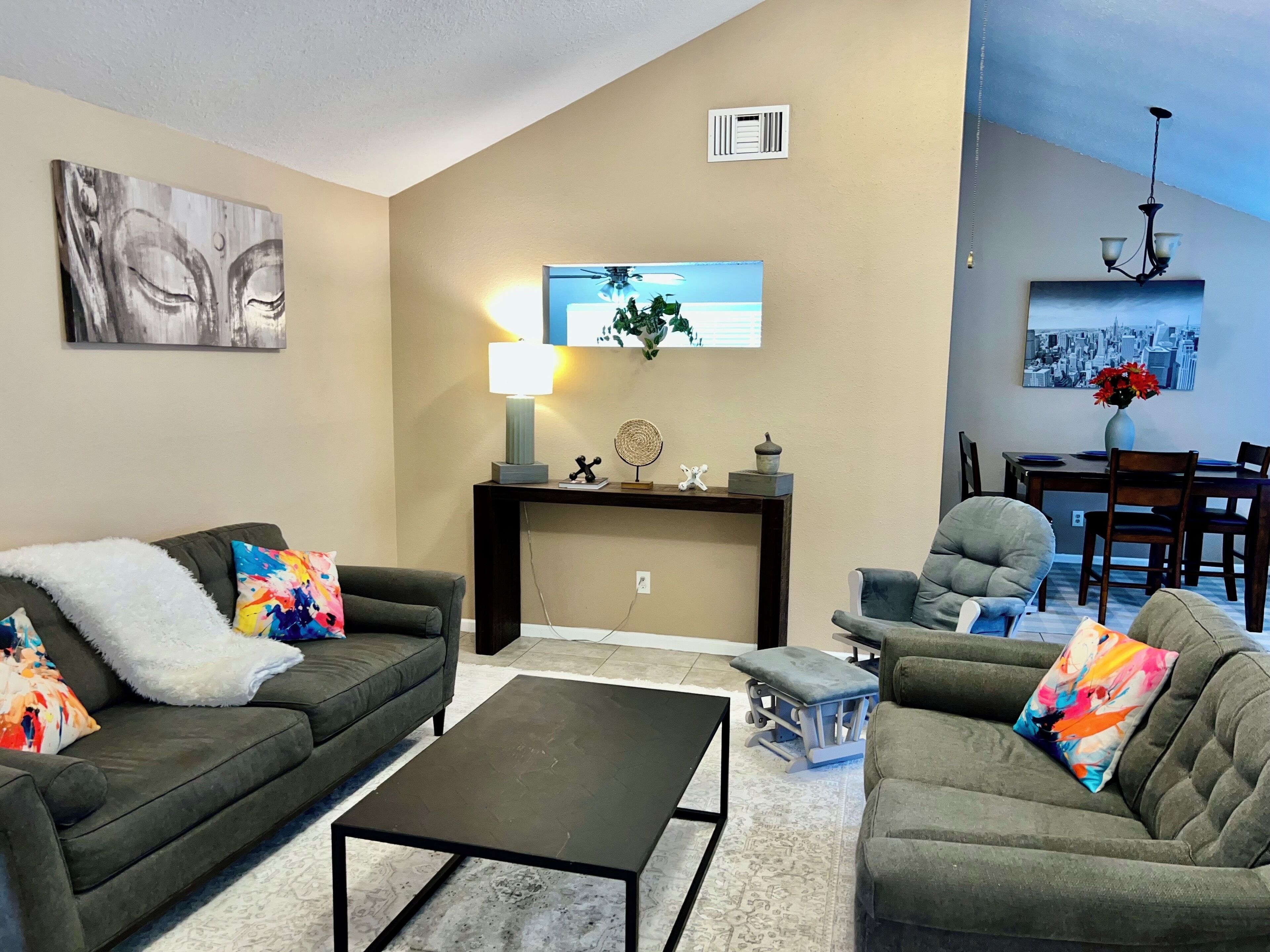 A living room with a sofa, a coffee table, a side table with a lamp, and a dining area with chairs and a table.