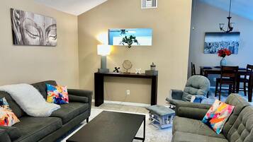 A living room with a sofa, a coffee table, a side table with a lamp, and a dining area with chairs and a table.