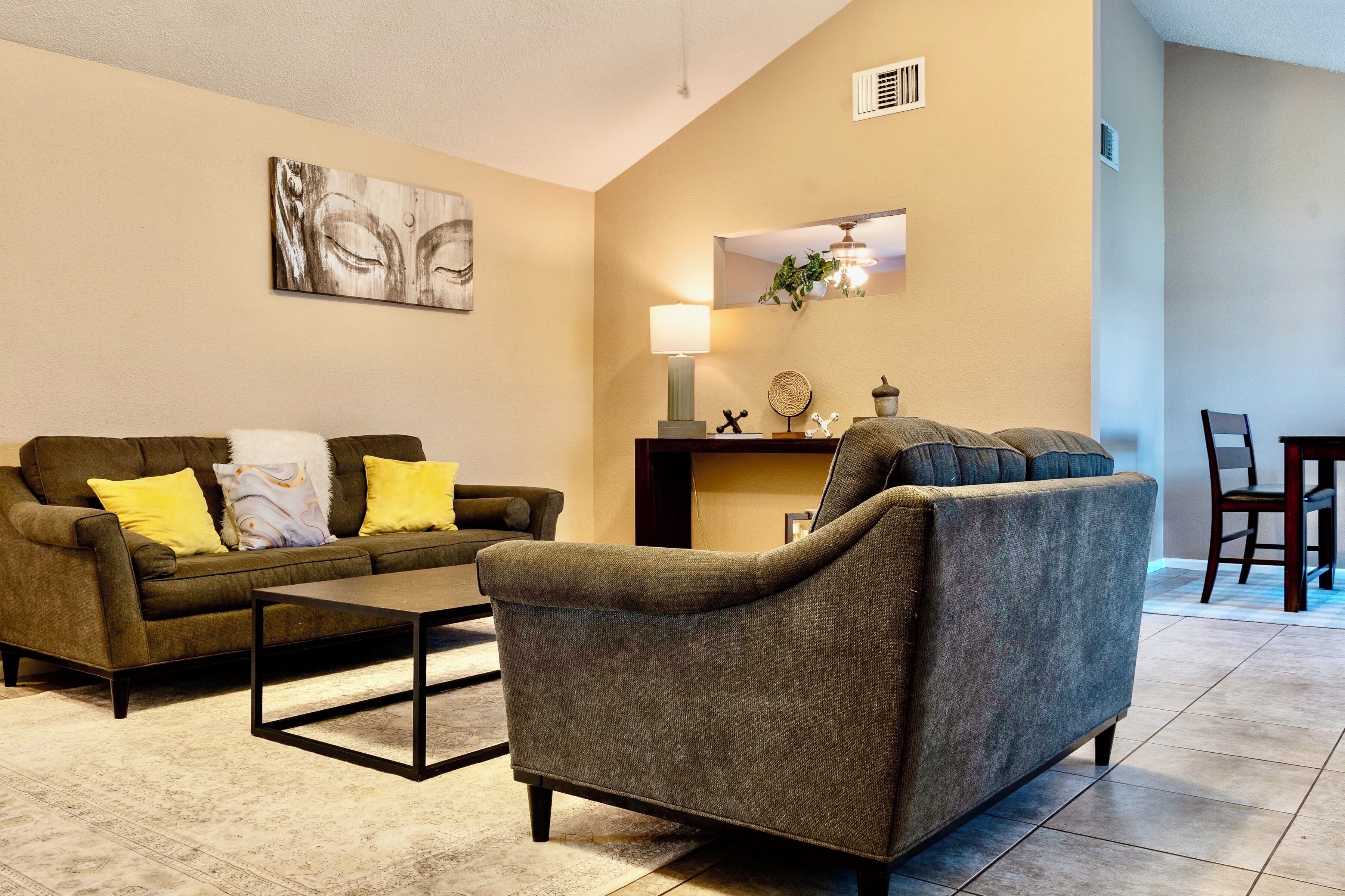 A living room with a sofa, armchair, coffee table, and a dining area with chairs and a table.