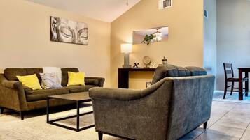 A living room with a sofa, armchair, coffee table, and a dining area with chairs and a table.