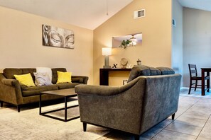 A living room with a sofa, armchair, coffee table, and a dining area with chairs and a table. - Katy Hideaway-FREE WI-FI/Fully Fenced Backyard (Katy)