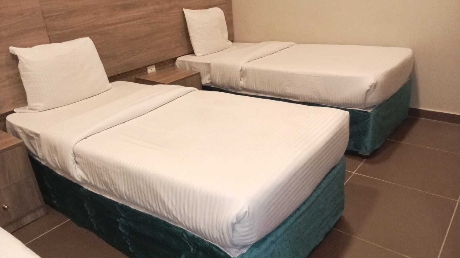 Two single beds with white linens, a wooden headboard, and a teal-colored bed skirt.