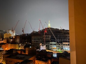 A nighttime view of a cityscape with multiple buildings under construction, featuring cranes and a prominent illuminated tower. - Rafef Aldyafa hotel (Makkah)