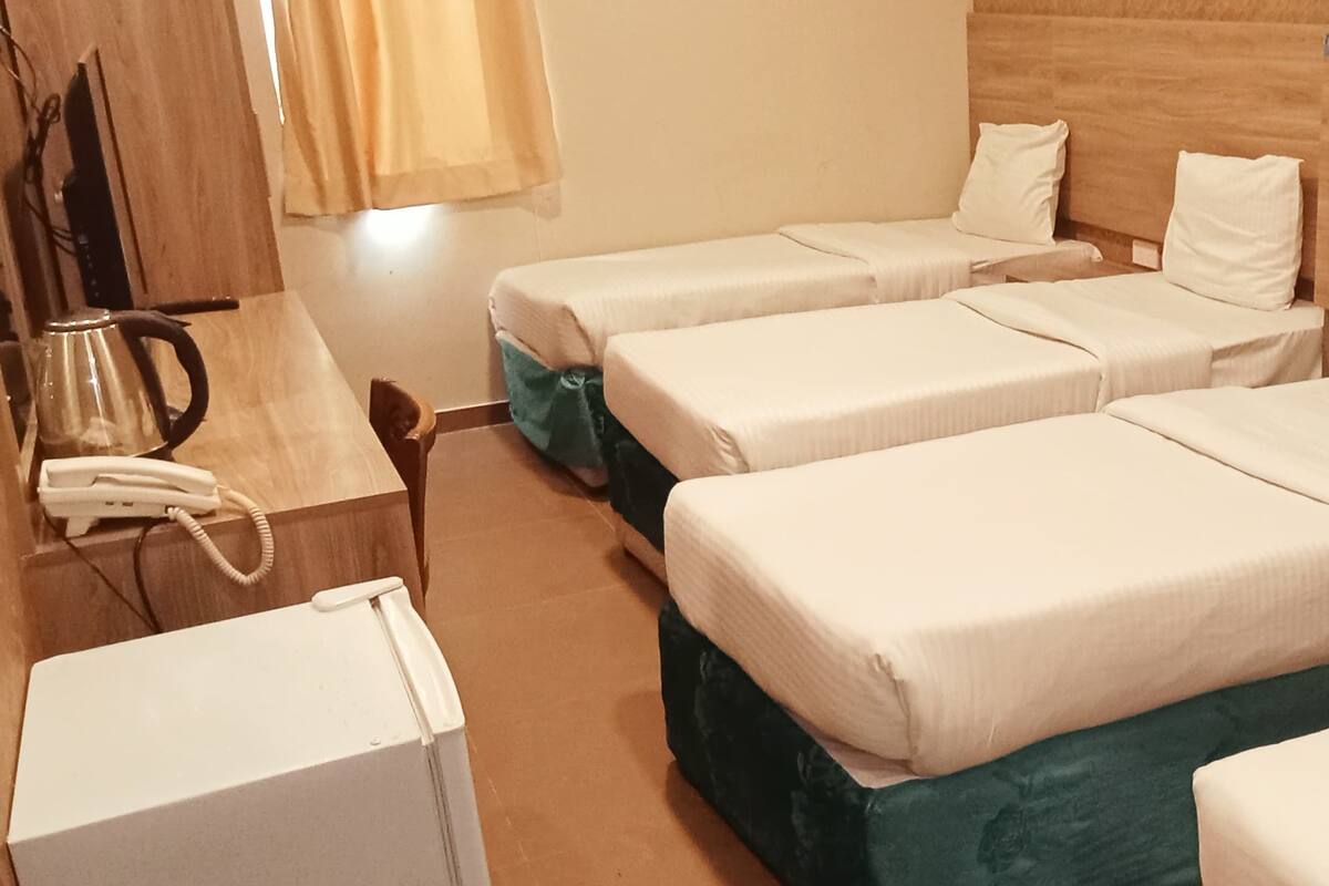 A room with four single beds, a wooden headboard, a small desk with a telephone, and a kettle.