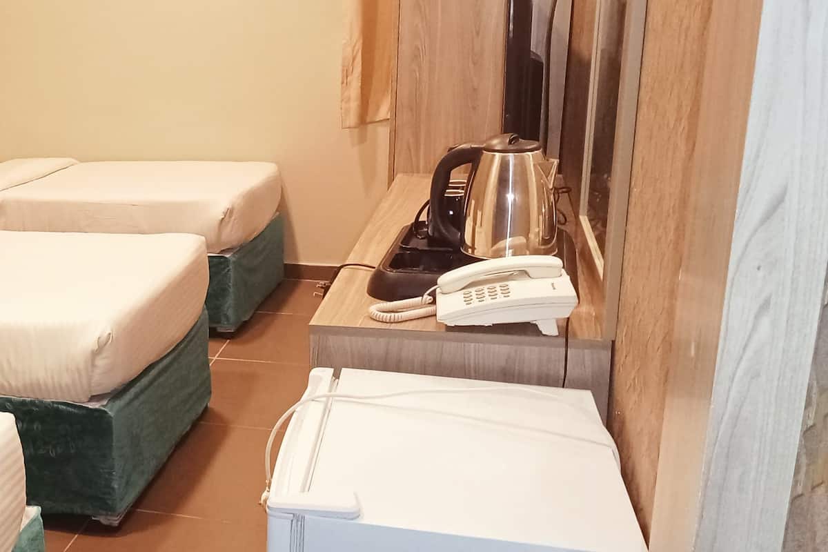 A hotel room with two beds, a desk with a telephone and kettle, and a small table.