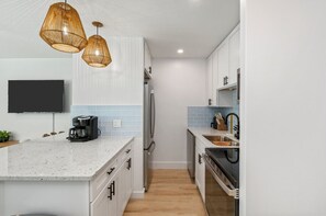 Una cocina moderna con armarios blancos, una isla grande, horno empotrado y cafetera.
