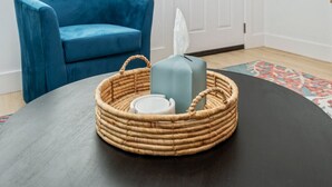 Een kamer met een blauwe fauteuil, een gevlochten mand met een zakdoekendoos en een witte container, en een kamerbreed tapijt met een patroon.
