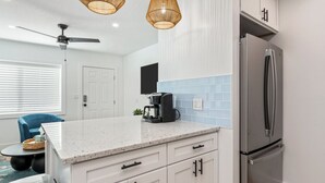Een moderne keuken met witte kastjes, een roestvrijstalen koelkast, een koffiezetapparaat en een plafondventilator.