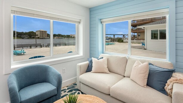 Un salon avec vue sur une plage et un bâtiment situé de l’autre côté de l’eau.