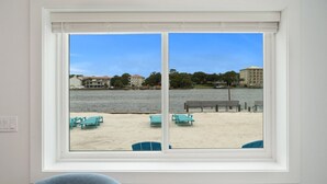 Une fenêtre donnant sur une plage, avec des chaises turquoise et un banc en bois.