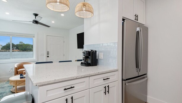 A modern kitchen with white cabinetry, stainless steel appliances, and wicker pendant lights. - Unit #5 Waterfront + Heated Pool and Spa Access (Fort Walton Beach)