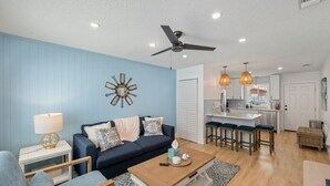 Una sala de estar con pared azul, ventilador de techo, una mesa de centro y un sofá.