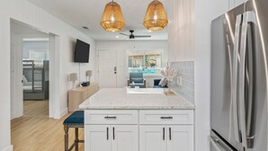 Una cocina moderna con muebles blancos, un refrigerador de acero inoxidable y un comedor con un banco.