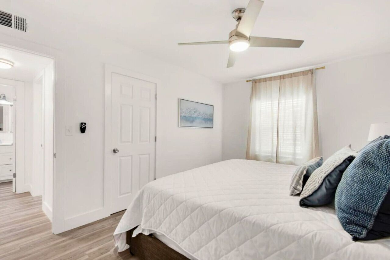 A bedroom with a bed, a ceiling fan, a door, and a window with curtains.