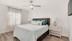 Ein Schlafzimmer mit einem Bett, Nachttischen, einem Deckenventilator und einem an der Wand befestigten Fernseher.