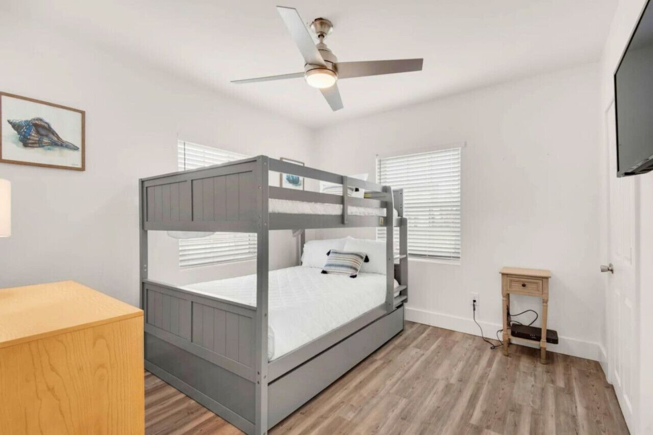 Ein Etagenbett mit Deckenventilator, ein kleiner Nachttisch aus Holz und ein gerahmtes Bild an der Wand.