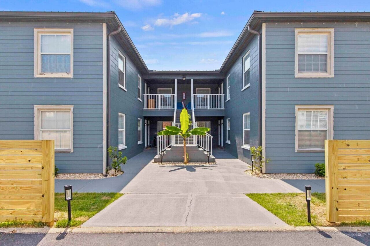 Un immeuble d’appartements à deux étages, doté d’une entrée centrale, d’un petit jardin et d’un portail en bois.