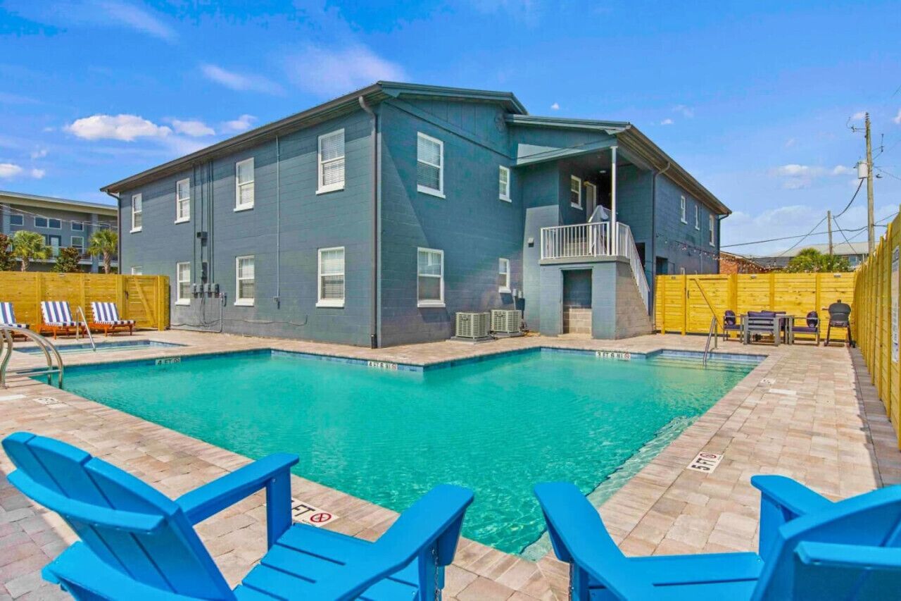 A building with a pool, blue chairs, and a yellow fence.