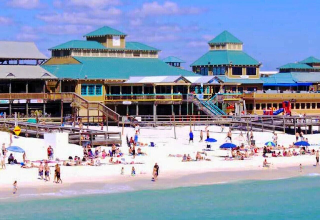 Un hotel frente a la playa con varias edificaciones, una playa de arena y un muelle.
