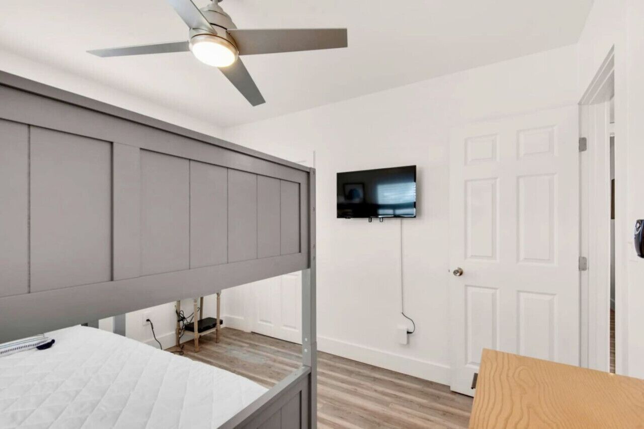 Un dormitorio con litera, ventilador de techo, televisor montado y una puerta blanca.