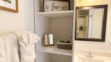 Un bany amb un lavabo blanc, un mirall, una estant amb un cartell que diu 'I love us', una planta penjant i un suport per a tovalloles.