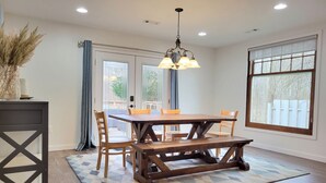 Een eetgedeelte met een houten tafel, stoelen, een vloerkleed met patroon en een hanglamp.