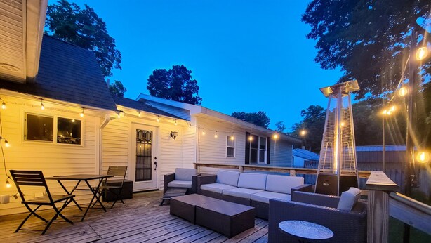 Een houten terras met buitenmeubilair, sfeerverlichting en een ladder.