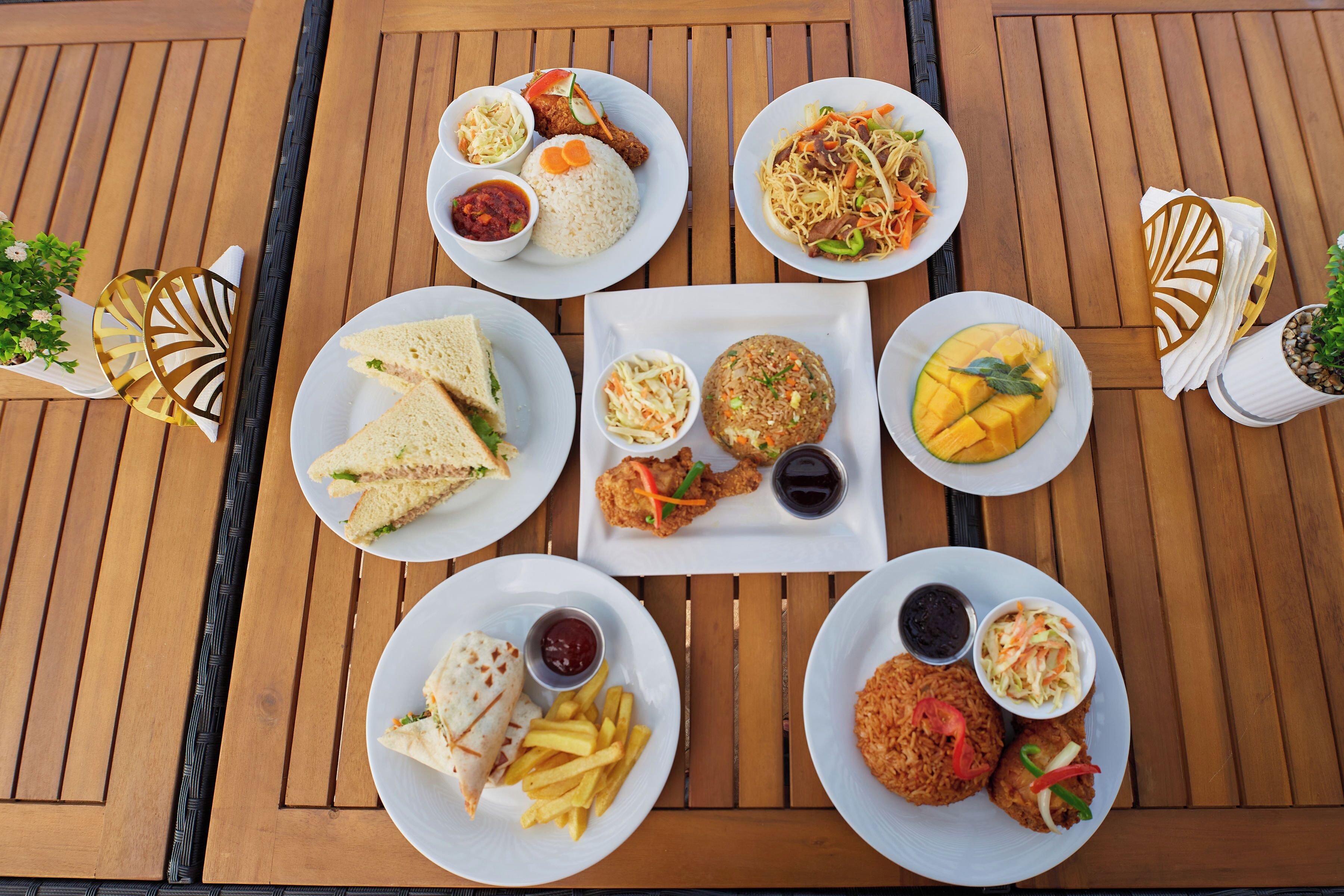 A wooden table with various dishes including rice, sandwiches, and fried items, arranged for a meal.