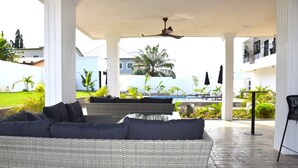 A covered outdoor seating area with a wicker sofa and a ceiling fan. - River Hills Hotel & Suites (Mile 11)