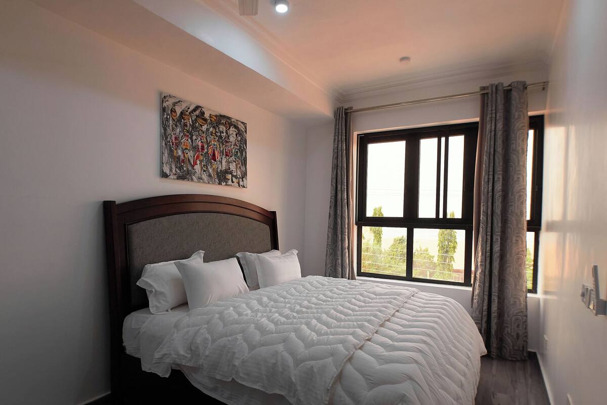 A bedroom with a bed, a ceiling fan, a window with curtains, and a painting on the wall.