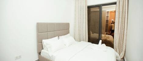 A hotel room with a bed, a wardrobe, and a sliding glass door leading to a balcony.