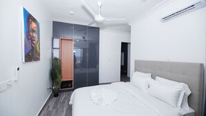 A modern bedroom with a bed, a ceiling fan, a wardrobe, and a painting on the wall. - River Hills Hotel & Suites (Mile 11)