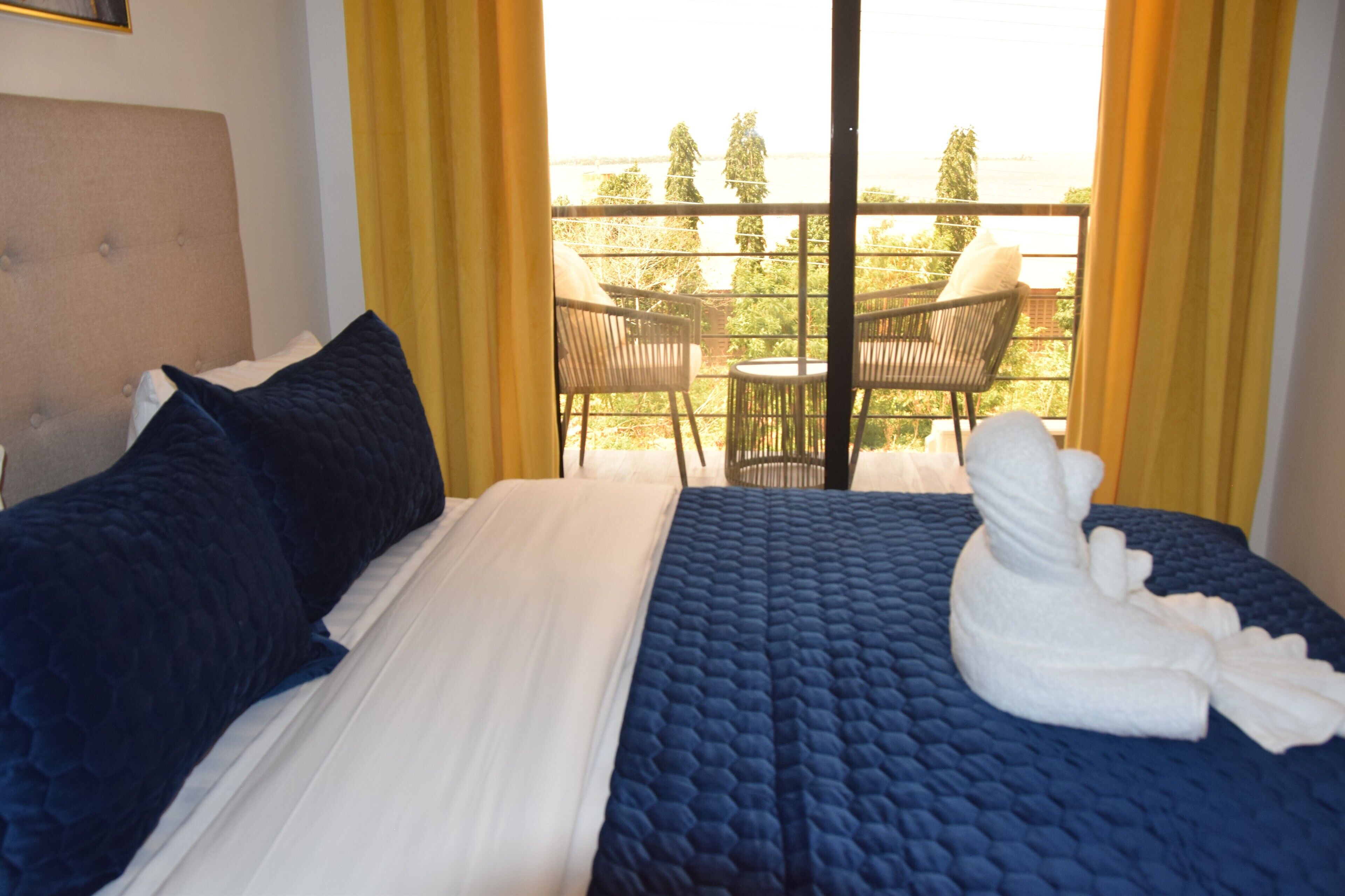 A hotel room with a bed, a window with yellow curtains, and a balcony with chairs and a table.
