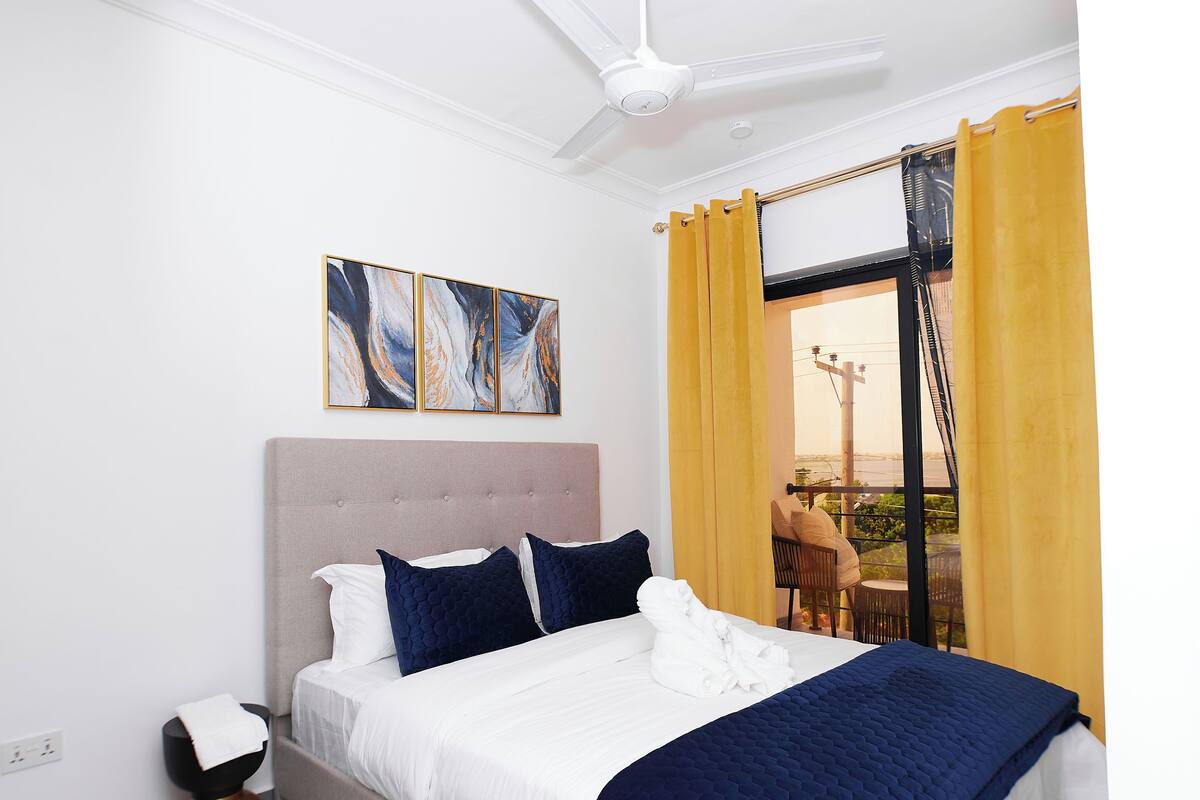 A modern bedroom with a bed, a ceiling fan, and artwork on the wall.