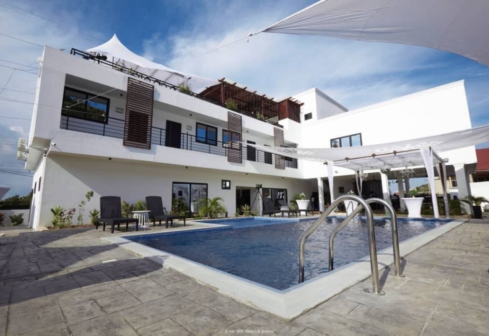 A modern hotel with a swimming pool, outdoor seating, and a covered area.