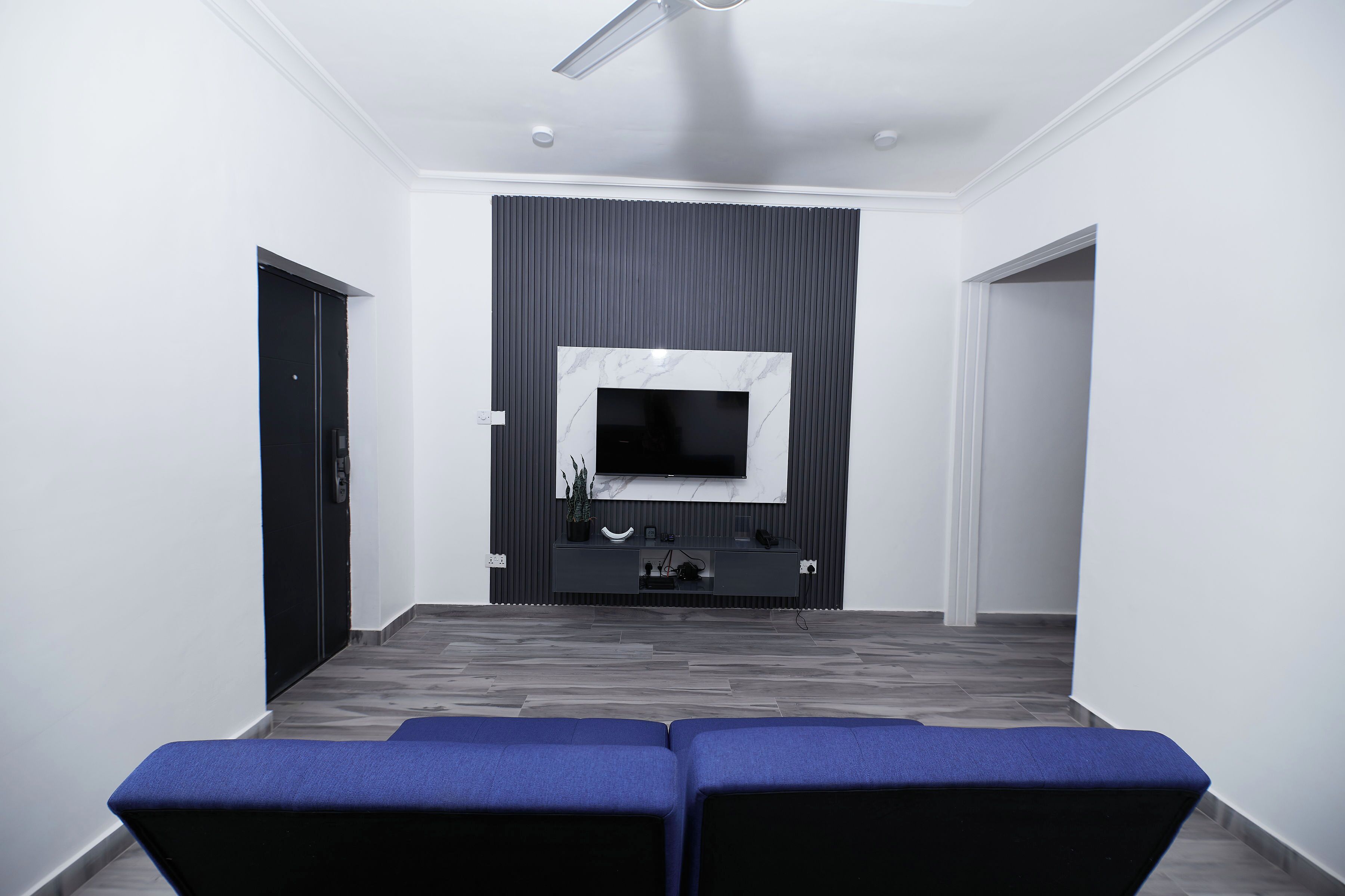 A modern living room with a flat-screen TV mounted on a dark wall, a wooden floor, and a blue bench in the foreground.