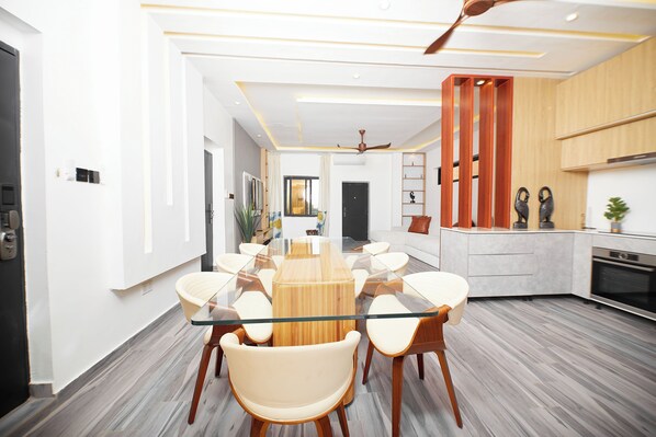 A modern kitchen with a central island, a dining area with a glass-top table, and a ceiling fan. - River Hills Hotel & Suites (Mile 11)