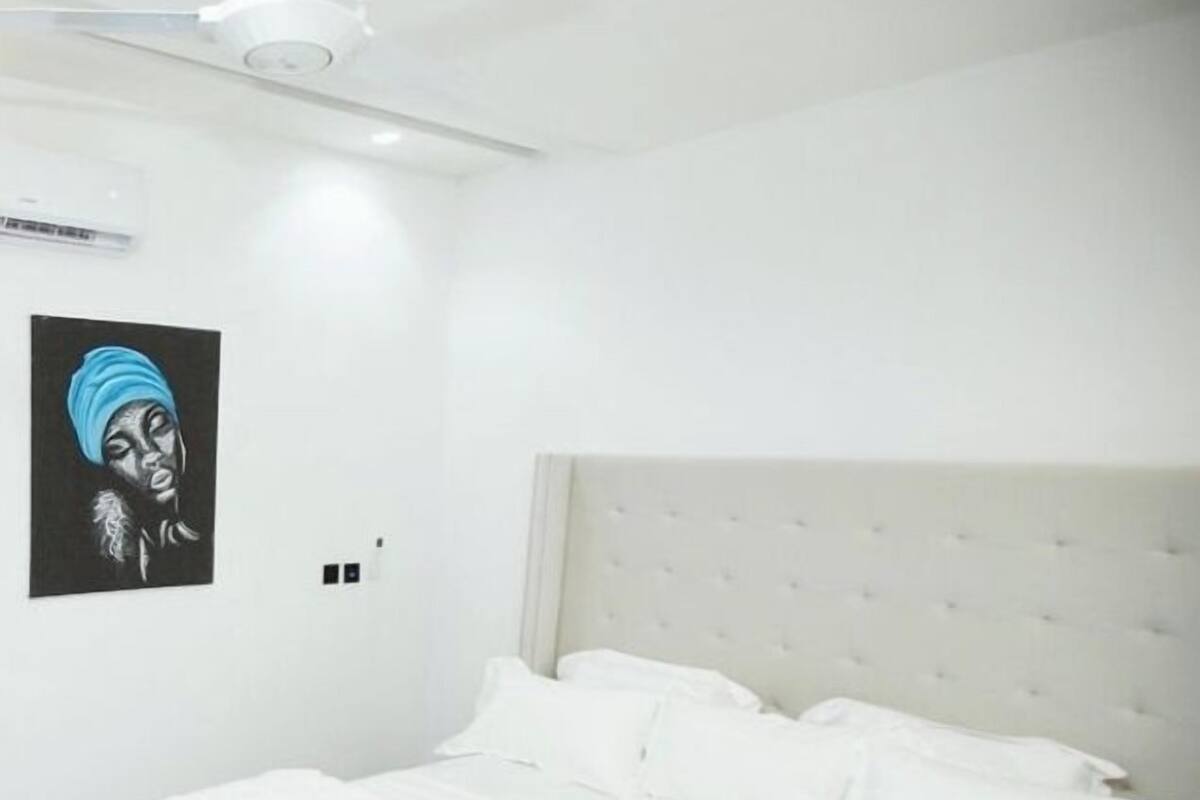 A bedroom with a large bed, white bedding, a headboard, a ceiling fan, and a wall-mounted light fixture.