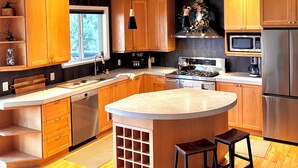 A modern kitchen with wooden cabinets, a large island, stainless steel appliances, and a window providing natural light.