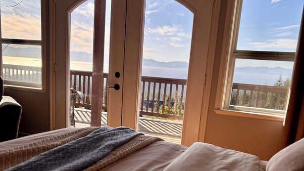 A bedroom with a bed, a window, and a view of a deck and mountains.