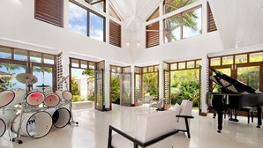 A spacious room with a grand piano, a drum set, and a white sofa.