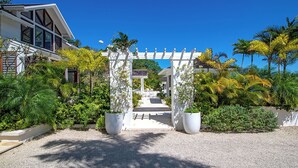 A modern house with a white exterior, a covered driveway, and lush tropical landscaping.