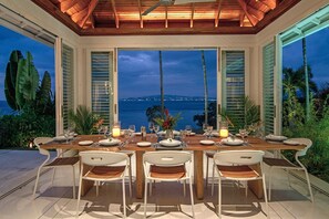 Un área de comedor al aire libre con vista al océano y al paisaje urbano al atardecer.