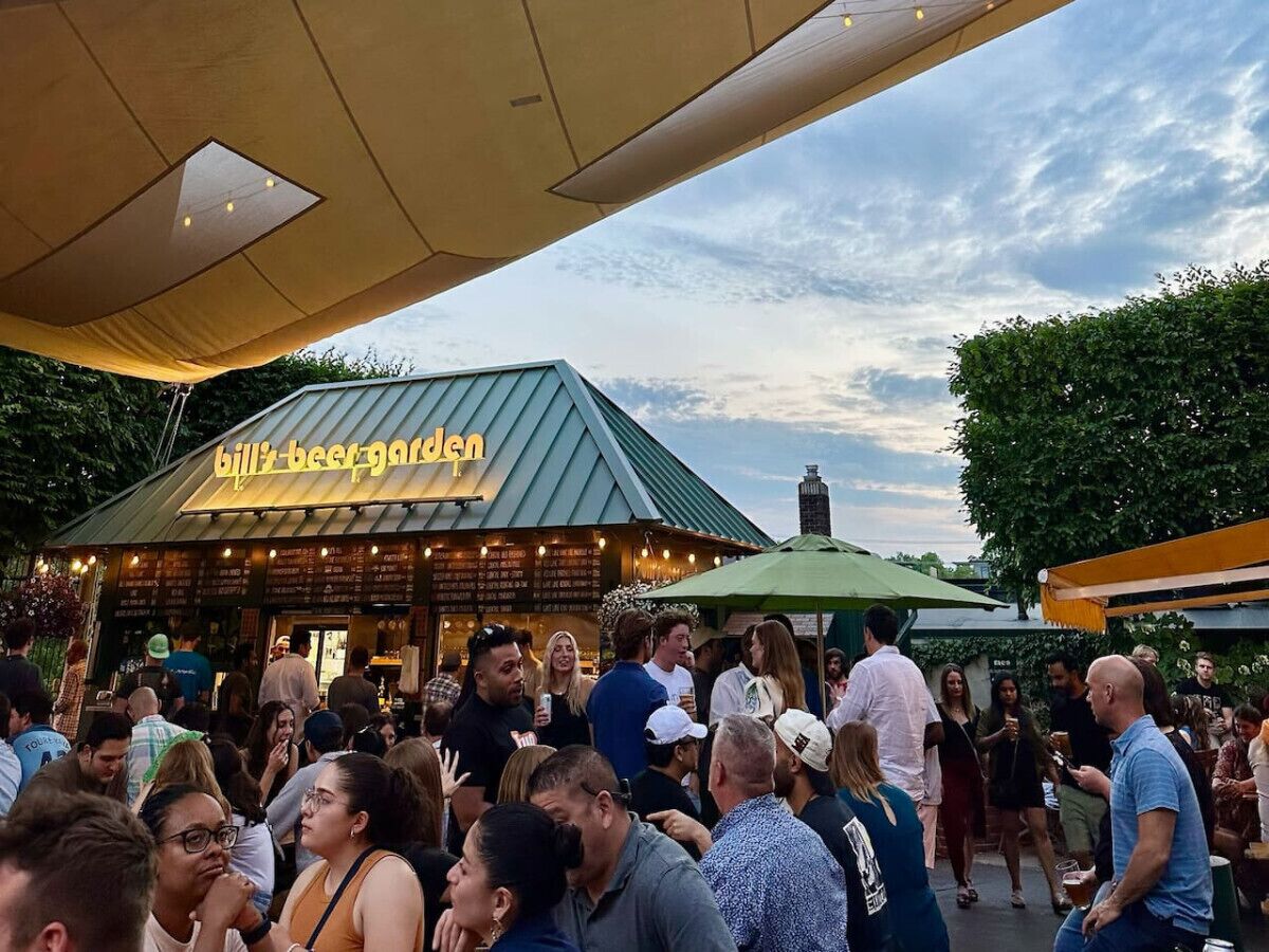 A crowded outdoor dining area with a restaurant named "Bill's Beer Garden" and a green-roofed building.