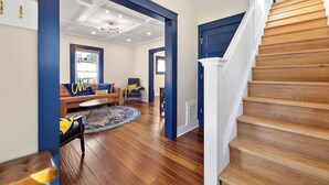 Un salón espacioso con piso de madera, pared de acento azul y una escalera que lleva al piso superior.