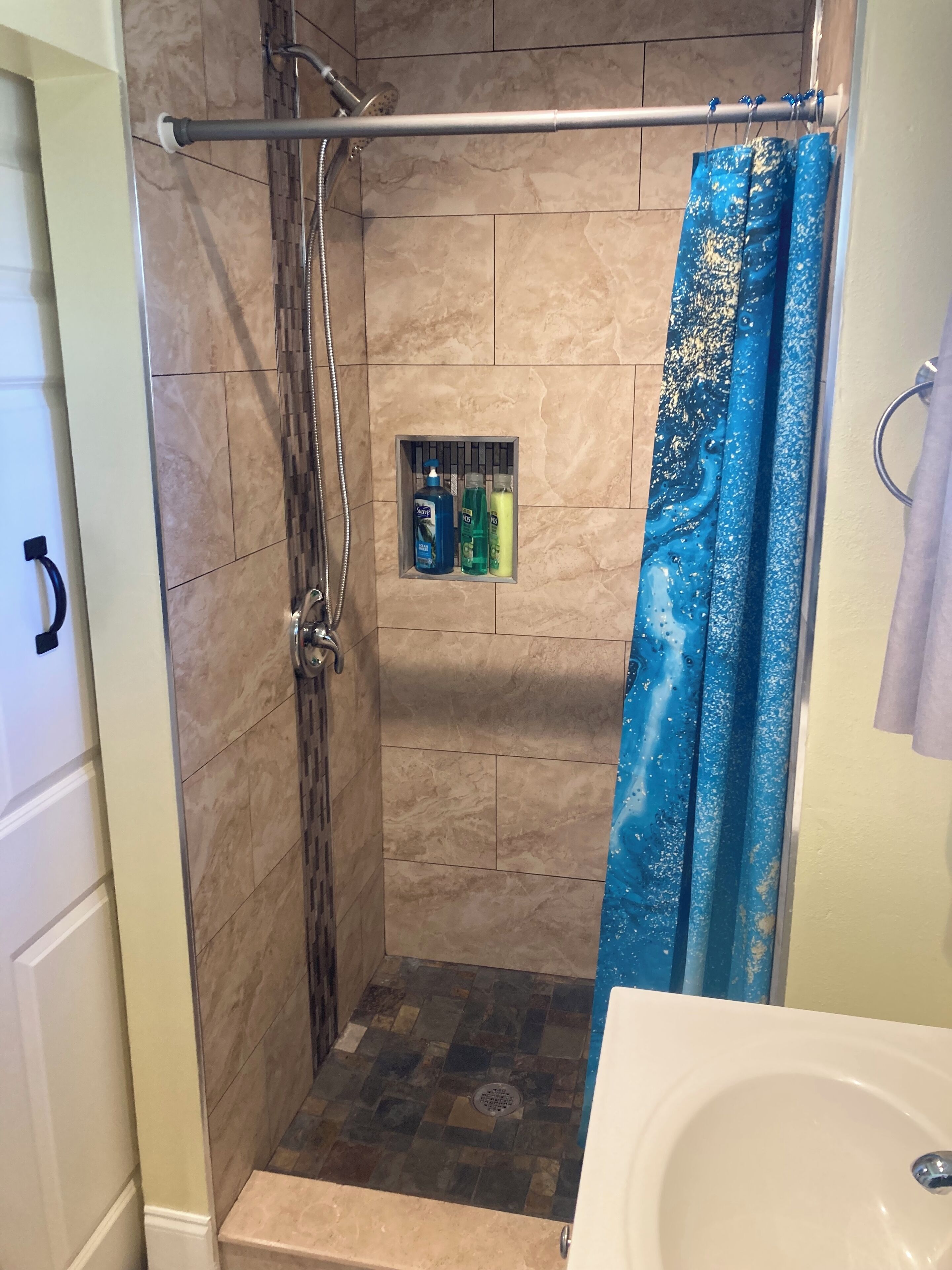 Une douche avec une porte en verre, un porte-serviettes et une étagère pour les articles de toilette.