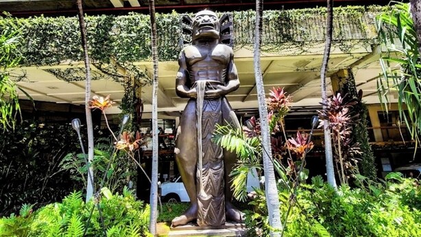 A statue in a tropical garden setting with a building in the background. - Beautiful OCEAN & CANAL View - Renovated - Waikiki Studio (Honolulu)